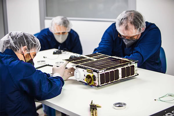 Two engineers dissect a cubesat with a third person watching
