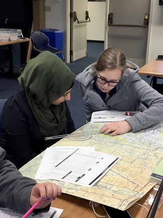 Two ASP students plot a course on a navigation chart.