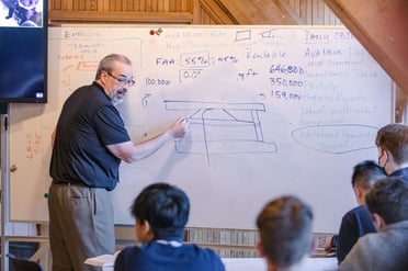 An ASP instructor demonstrates a principal of aviation on a whiteboard.