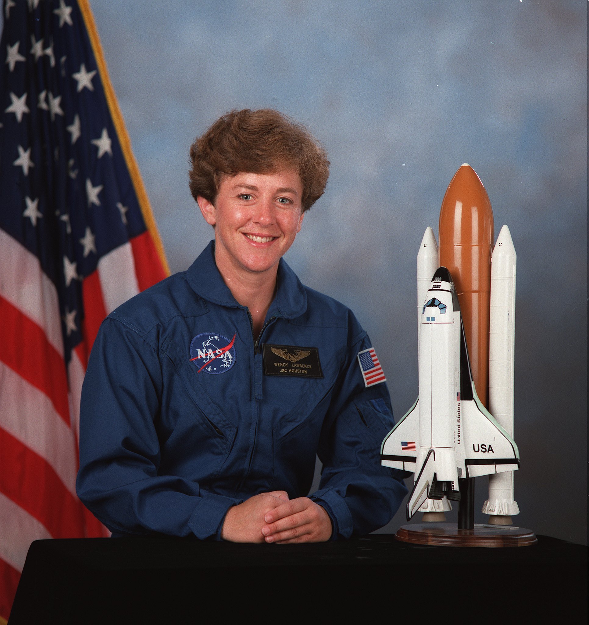 Featured image: Astronaut Wendy Lawrence sits for her official crew photo. A model of the Space Shuttle sits on her right, and an American flag on her left. - Read full post: Astronaut Wendy Lawrence